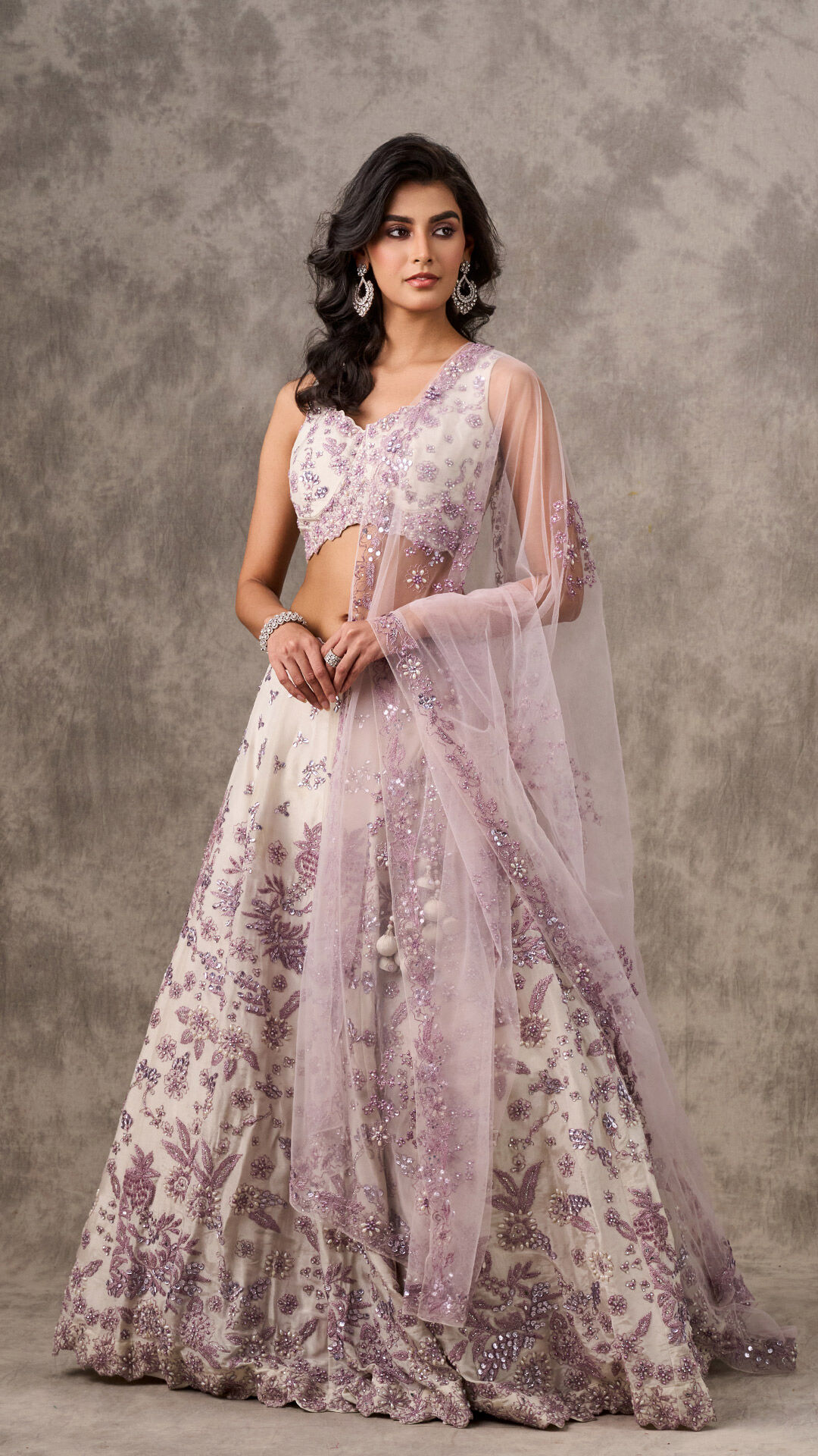 Woman in an embroidered white lehenga with purple floral threadwork and a sheer lavender dupatta.